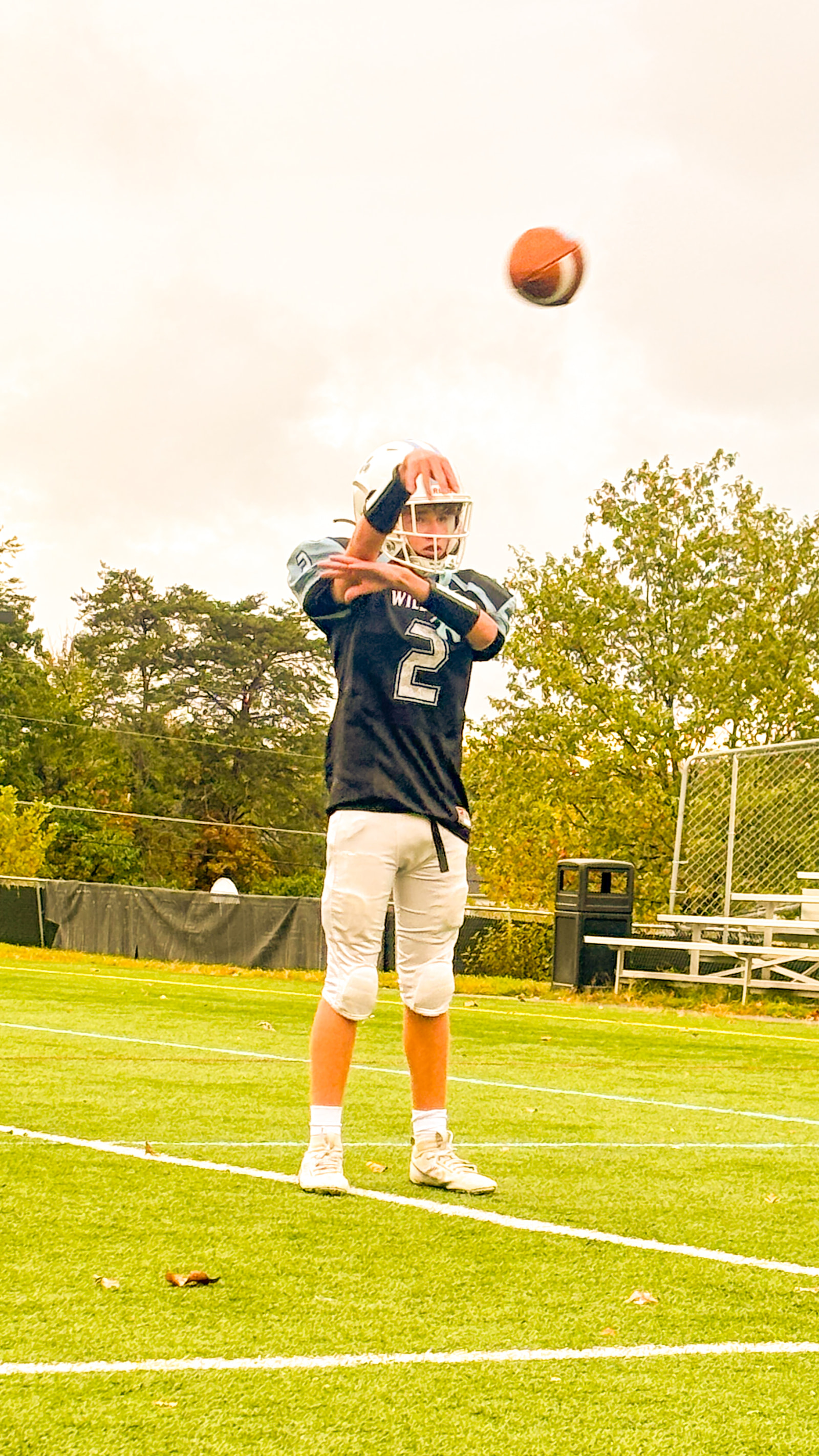 A young athlete in a football uniform prepares to catch a ball on a grassy field.