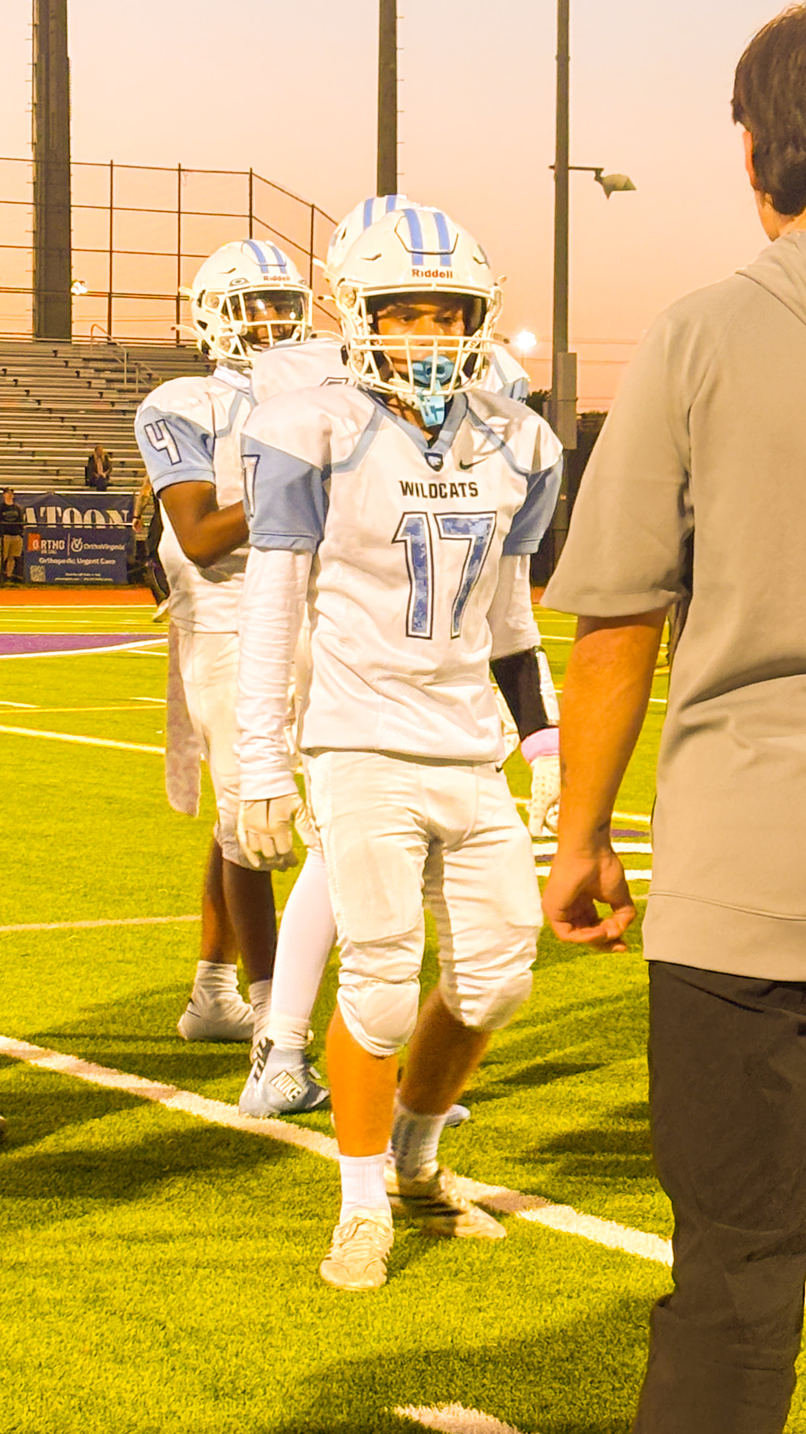 Two football players in white and light blue uniforms stand on a field, one wearing the number 17 jersey.