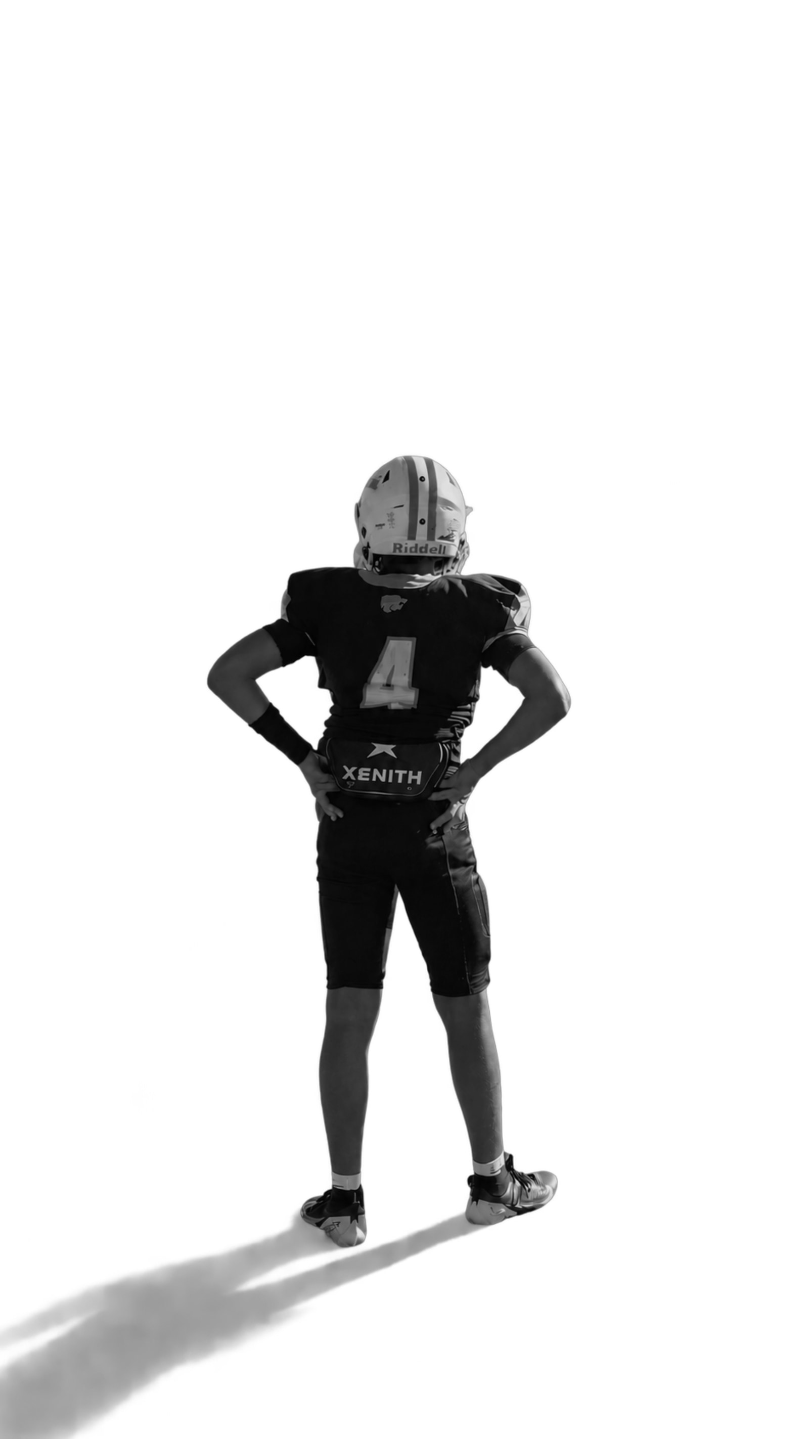A football player stands with hands on hips, facing away from the camera.