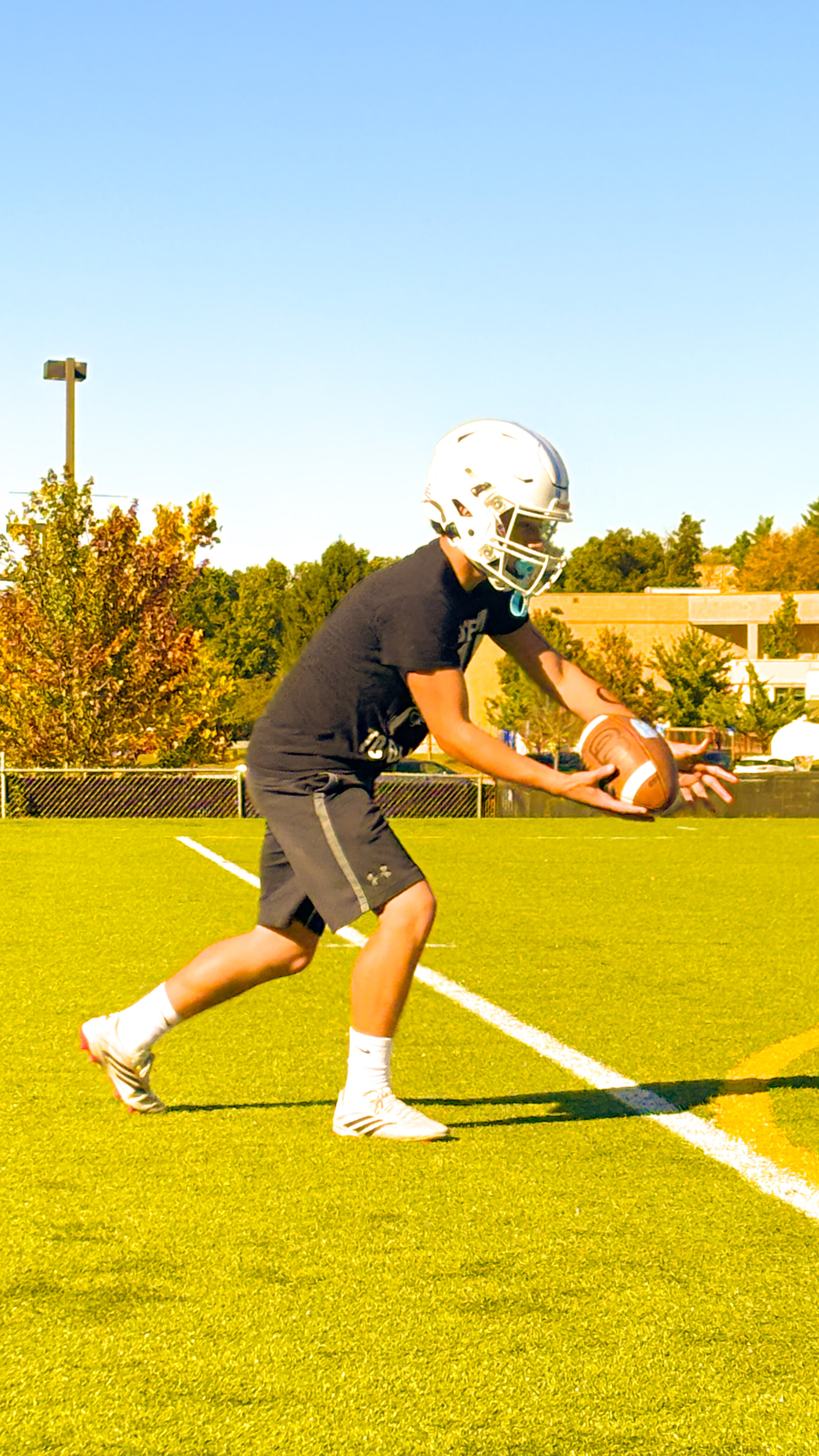 A young athlete in a helmet and jersey practices a football throw on a field.