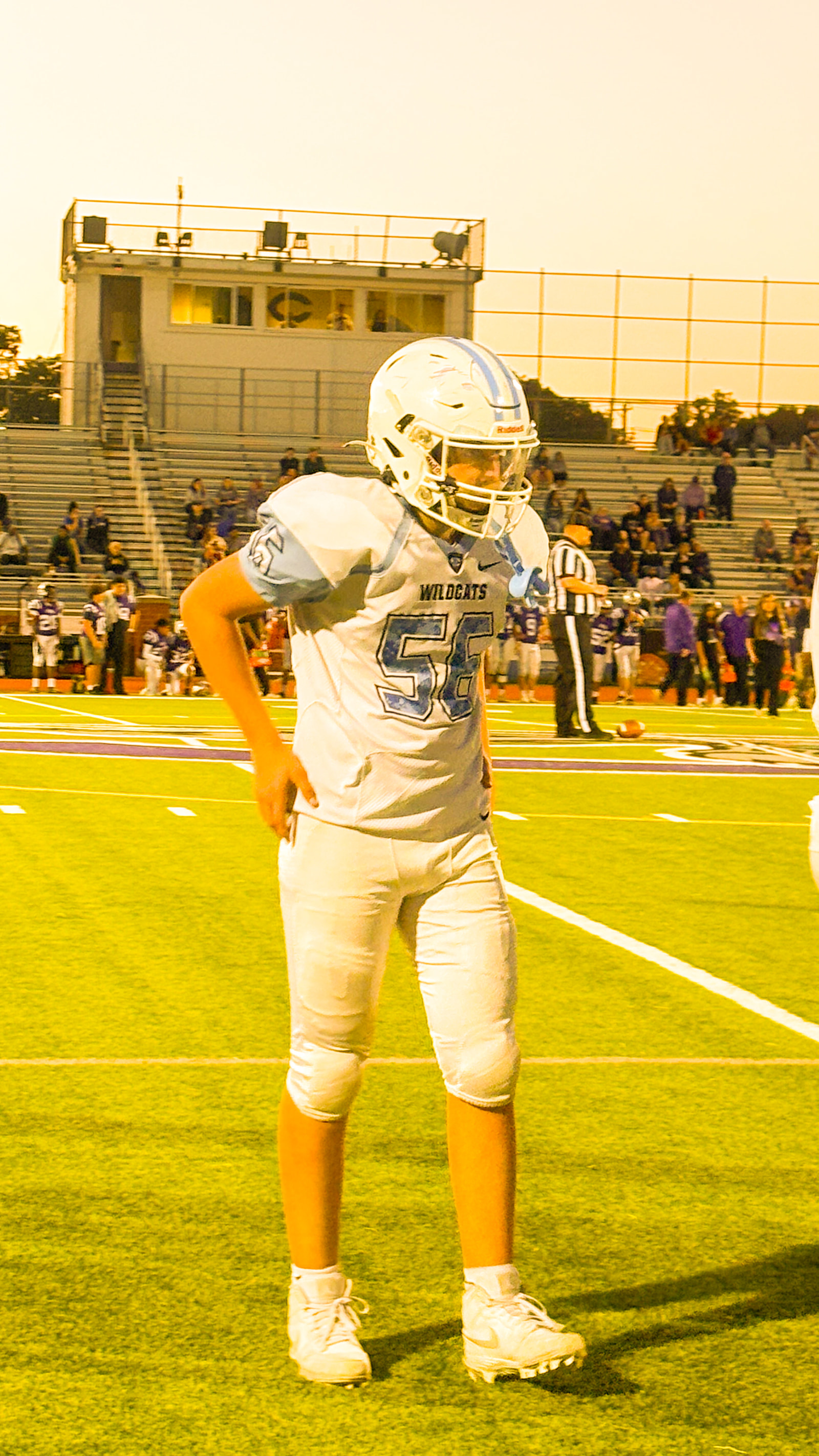 A football player stands on the field during a game, wearing a white jersey with the number 56 and a helmet.