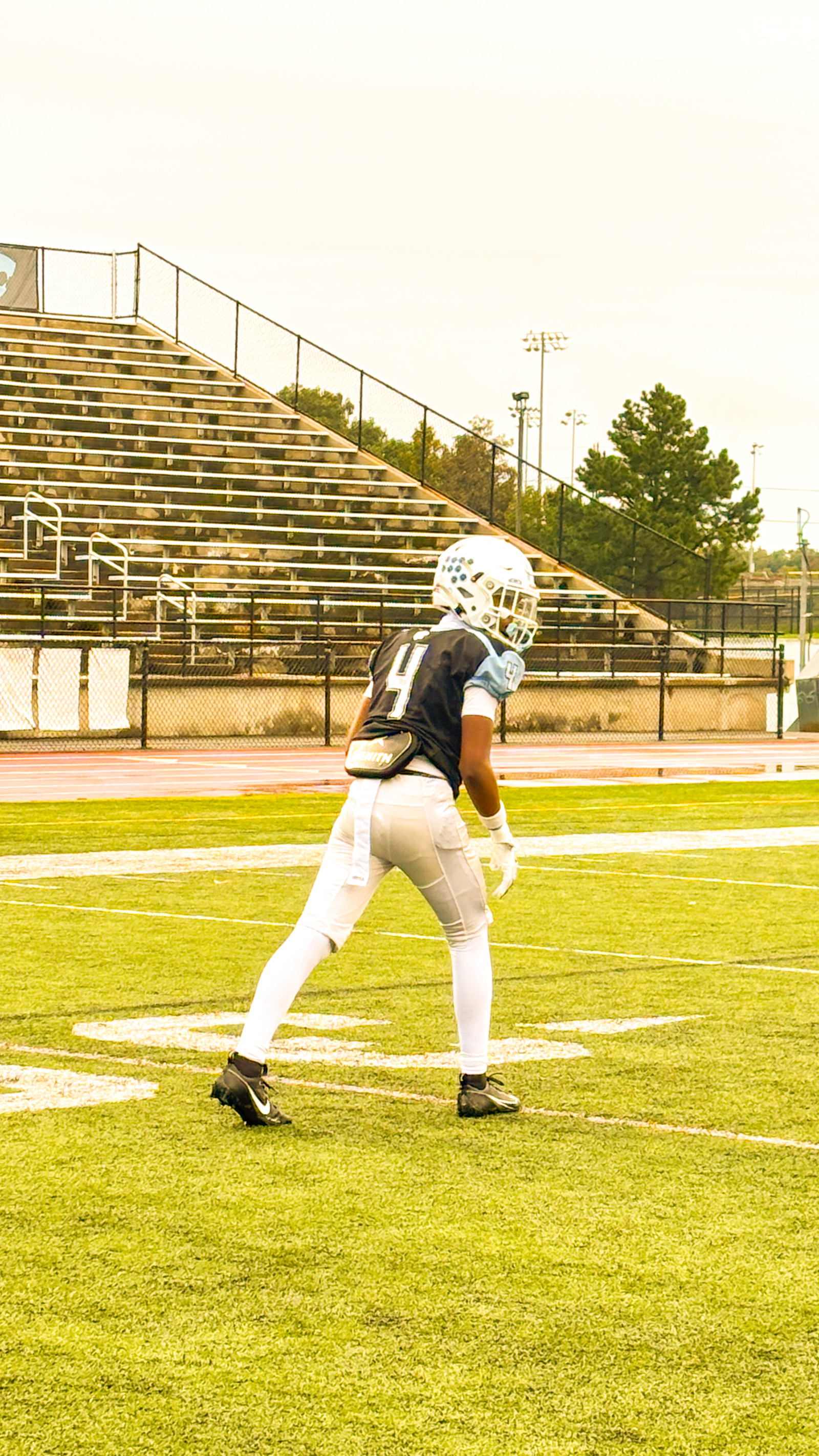 A football player in a black jersey and white helmet stands on a field, facing away from the camera.