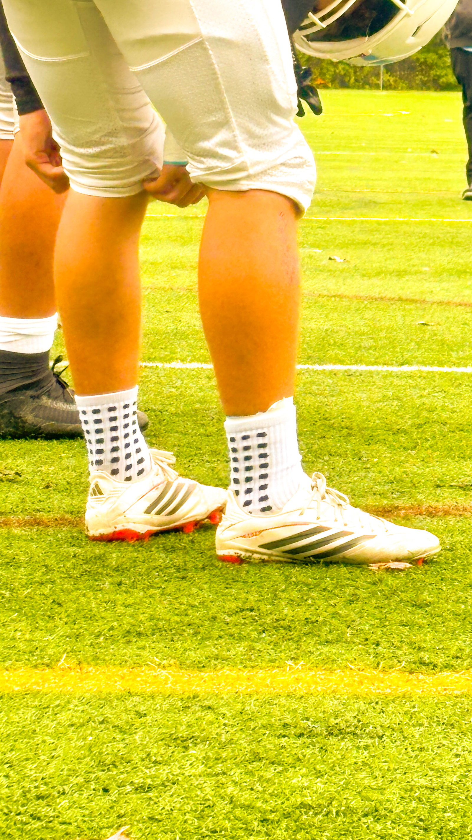 Close-up of a football player's lower legs and feet, showing cleats and socks on a grassy field.