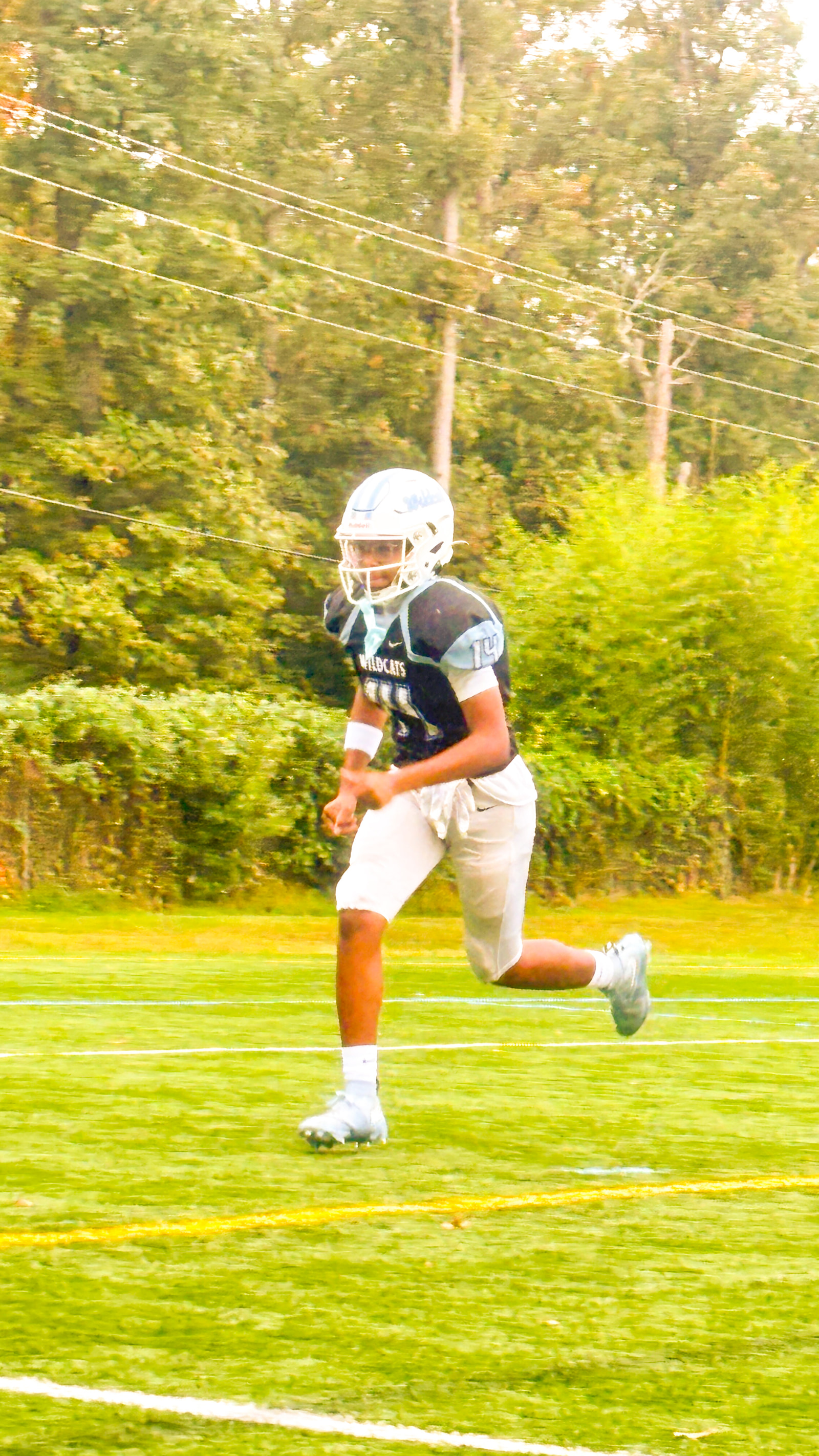 A young athlete in a football uniform runs on a grassy field during practice.